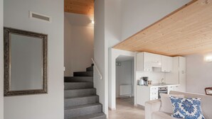 Un intérieur moderne avec un escalier menant à une cuisine, un canapé blanc agrémenté d’un coussin à motifs et un grand miroir encadré accroché au mur.