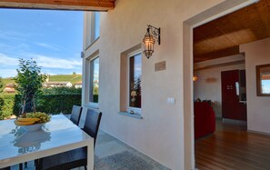 A dining area with a table and chairs, a bowl of fruit, and a view of the countryside.