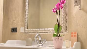 Ein Badezimmer mit Waschbecken, Spiegel und Dekoration, darunter eine rosa Orchidee in einem gemusterten Topf.