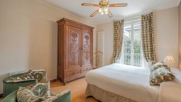 A bedroom with a bed, a wooden wardrobe, a green armchair, and a ceiling fan.