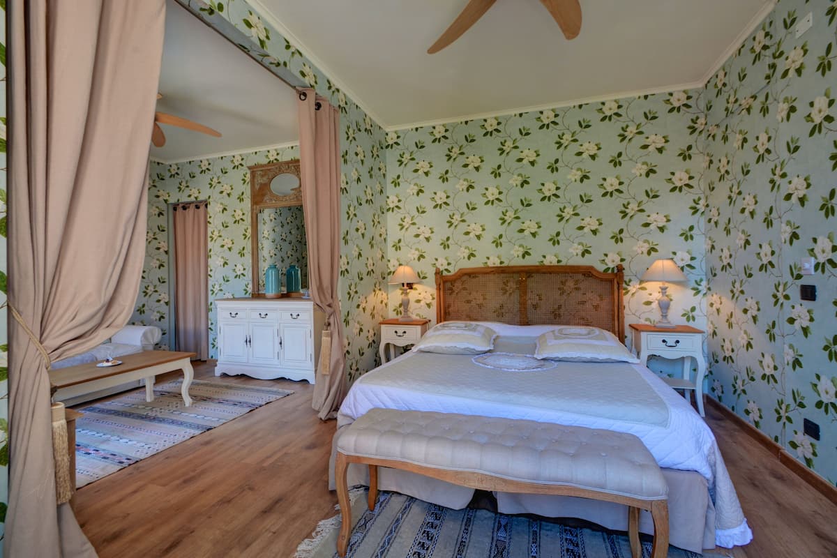 Un dormitorio con una cama grande, cabecera de madera, mesita de noche con lámpara, un banco, armario y espejo.