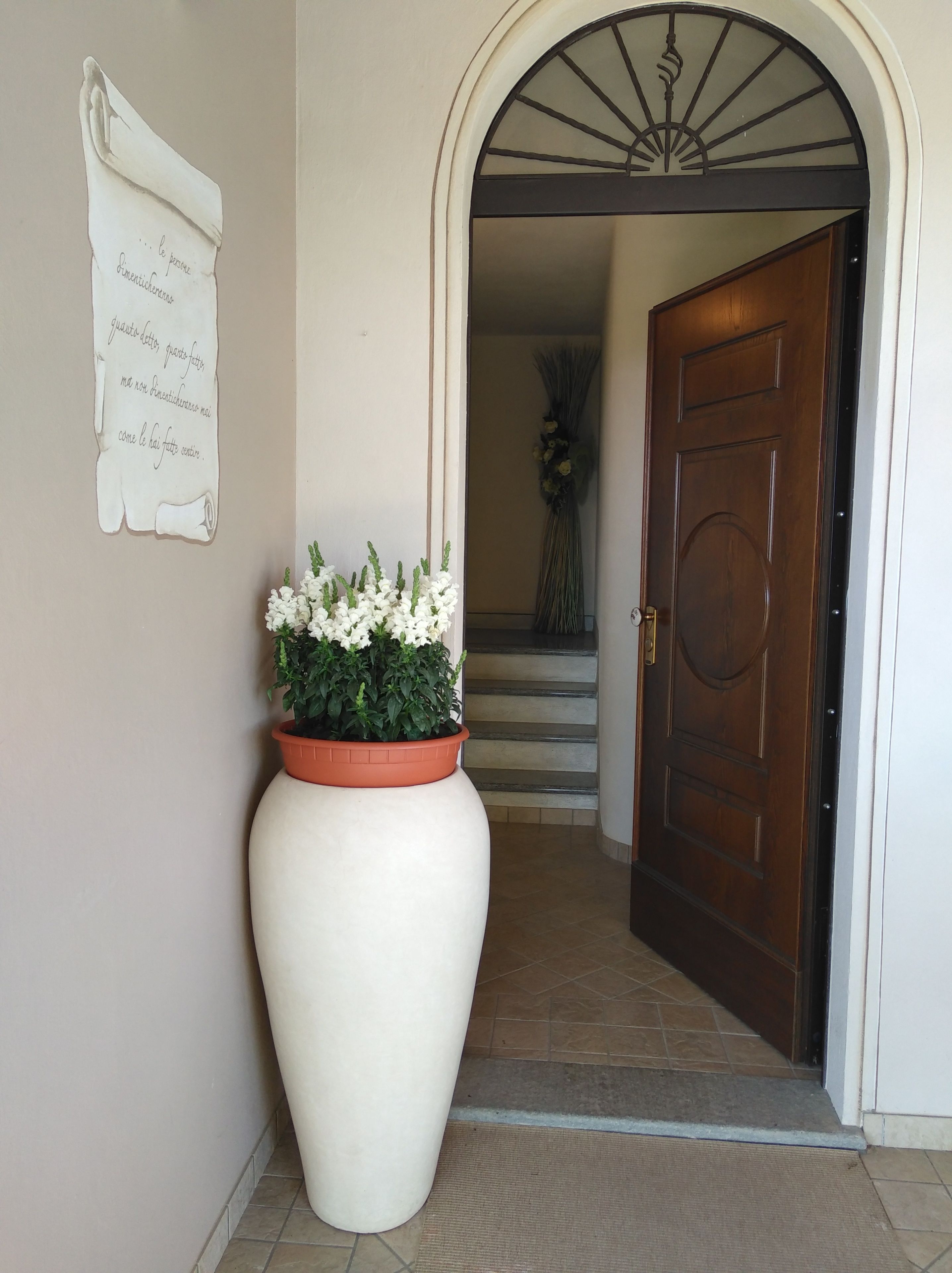 A hallway with a large white planter with white flowers, a wooden door, and a staircase in the background.