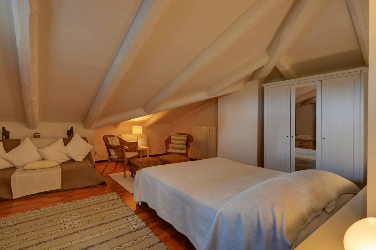 Acogedor dormitorio en el ático con cama, dos sillones, una mesita y un armario.
