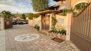 A gated entrance with a paved driveway leading to a building with a mural and a large window. - La Rosa Gialla (Barolo)