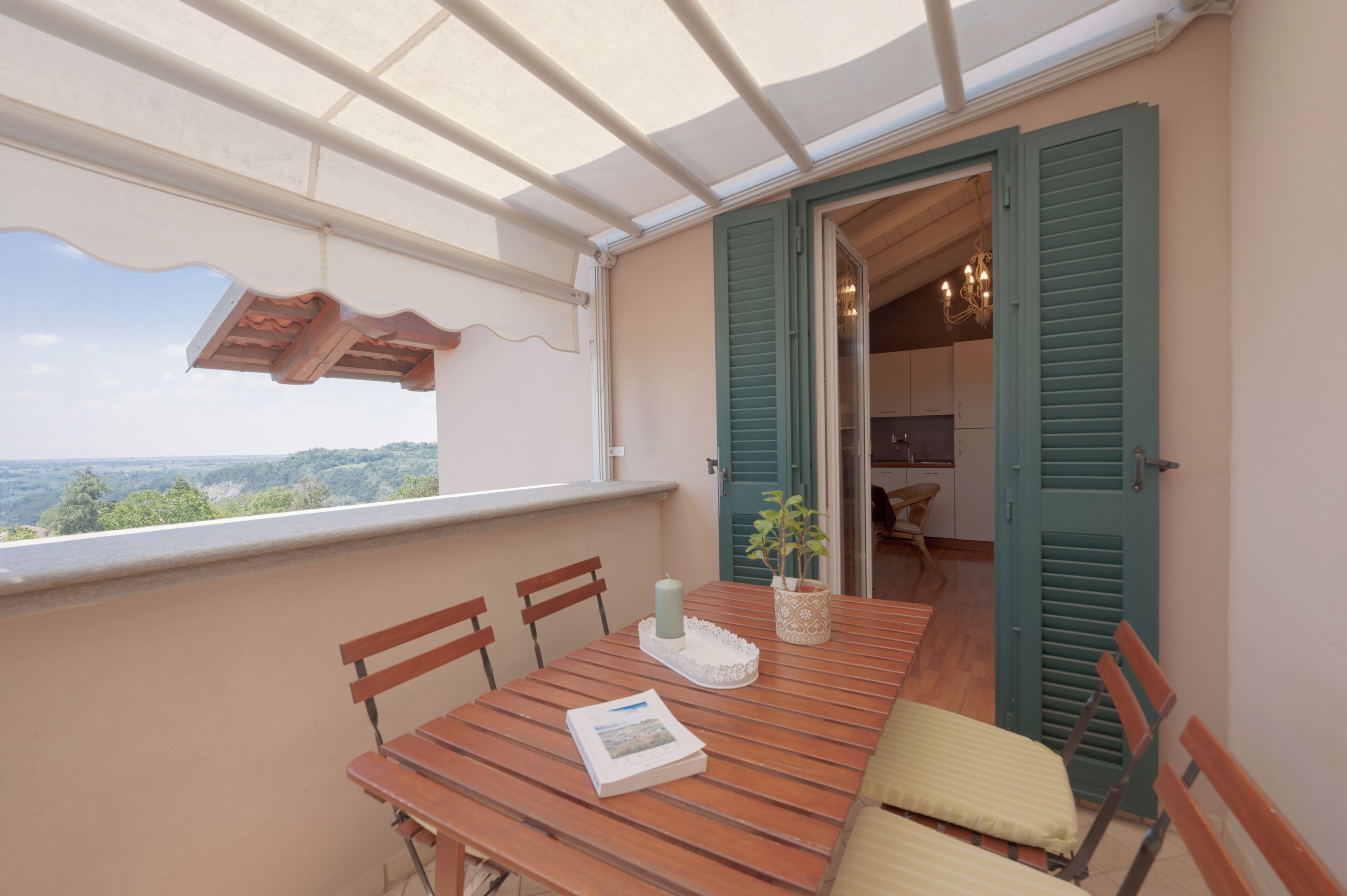 A balcony with a wooden table, chairs, a candle, and a potted plant.