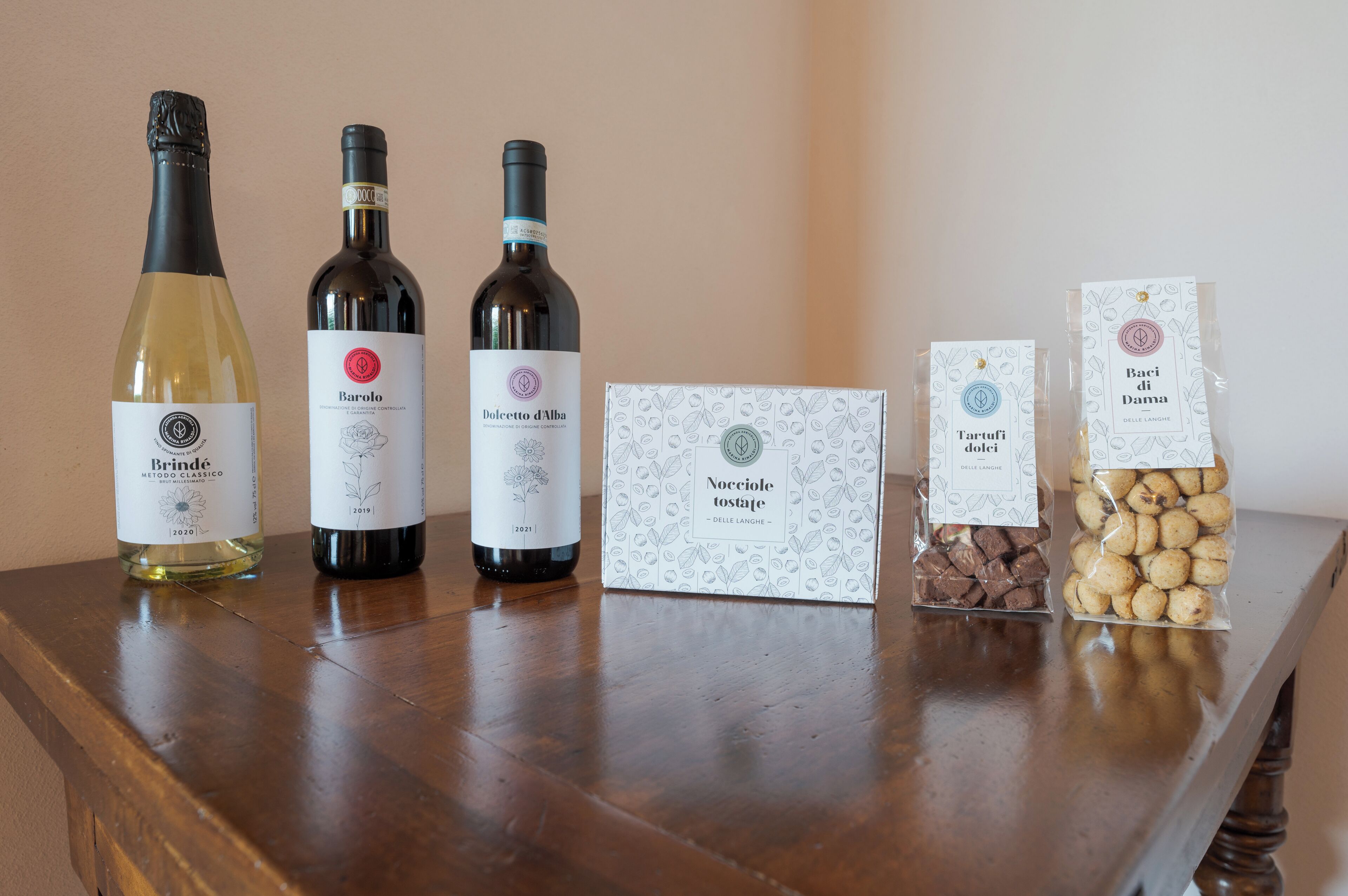 Three wine bottles and two packaged food items on a wooden table.