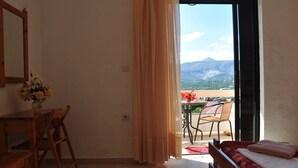 Una stanza con un letto, una scrivania in legno e una sedia. Si vede una finestra con tende e un balcone con mobili da esterno.