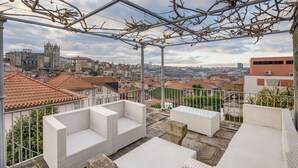 A balcony with white wicker furniture, a metal railing, and a view of a cityscape with buildings and a church. - OCA Flores Hotel Boutique (Porto)