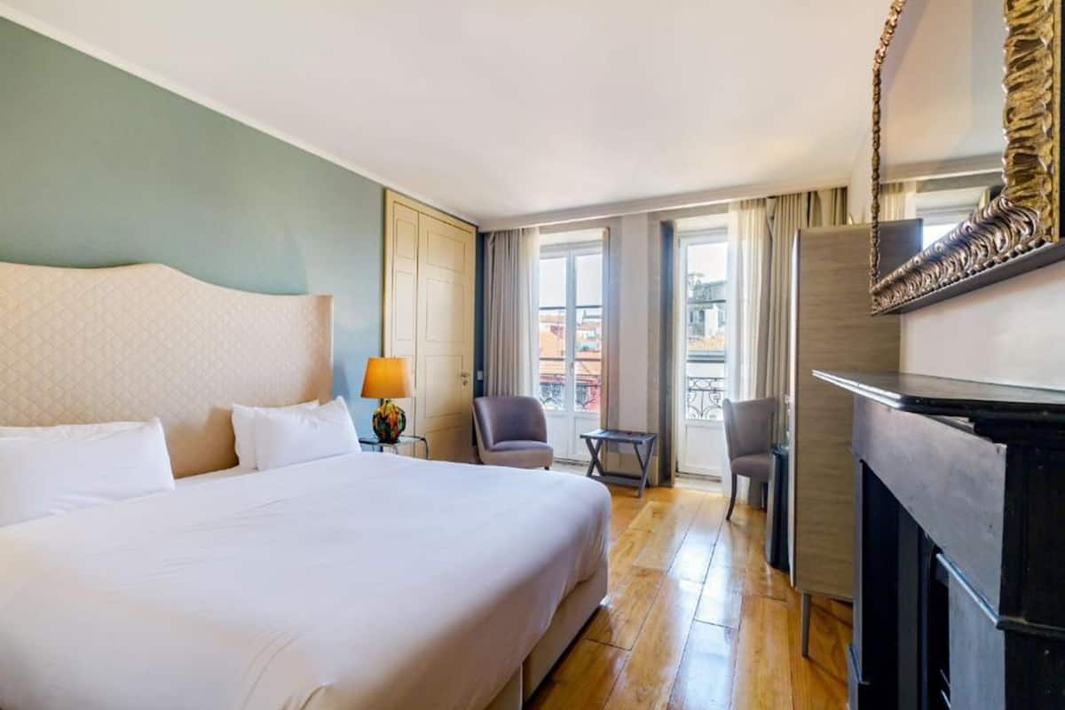 A hotel room with a large bed, a desk, a chair, a TV, and a balcony with curtains.