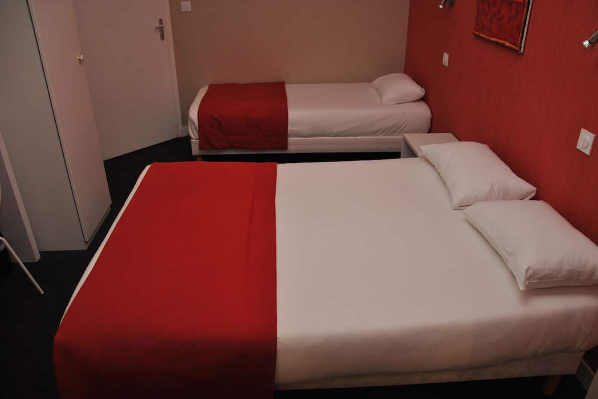 Une chambre d’hôtel avec deux lits, dont un plus grand et un plus petit, tous deux dotés de draps blancs et agrémentés de touches de couleur rouge.