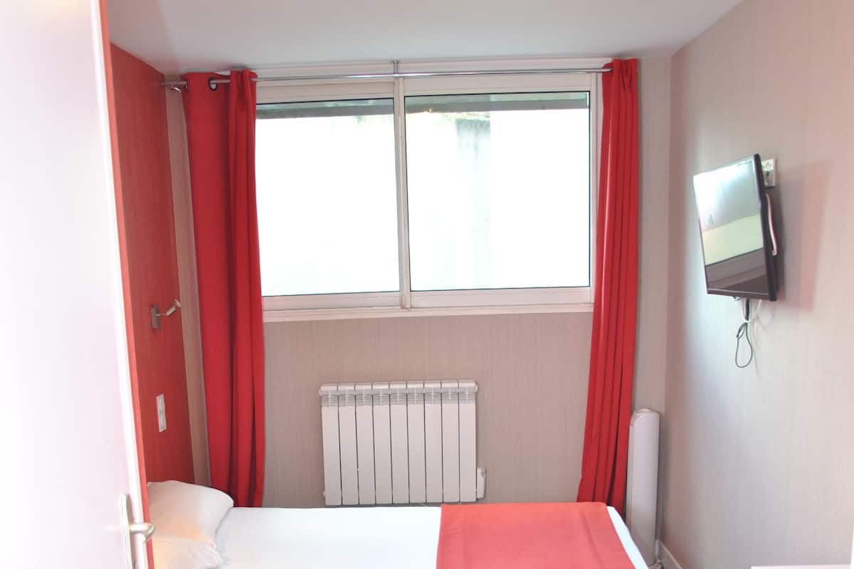 Une chambre d’hôtel avec un lit, un bureau, une télévision et une fenêtre avec des rideaux.