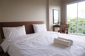 Una cama bien hecha con sábanas y almohadas blancas, cabecera de madera y ventana con vistas a la vegetación.