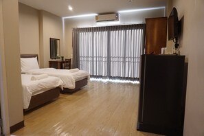 A hotel room with two beds, a desk, a chair, a television, and an air conditioning unit.