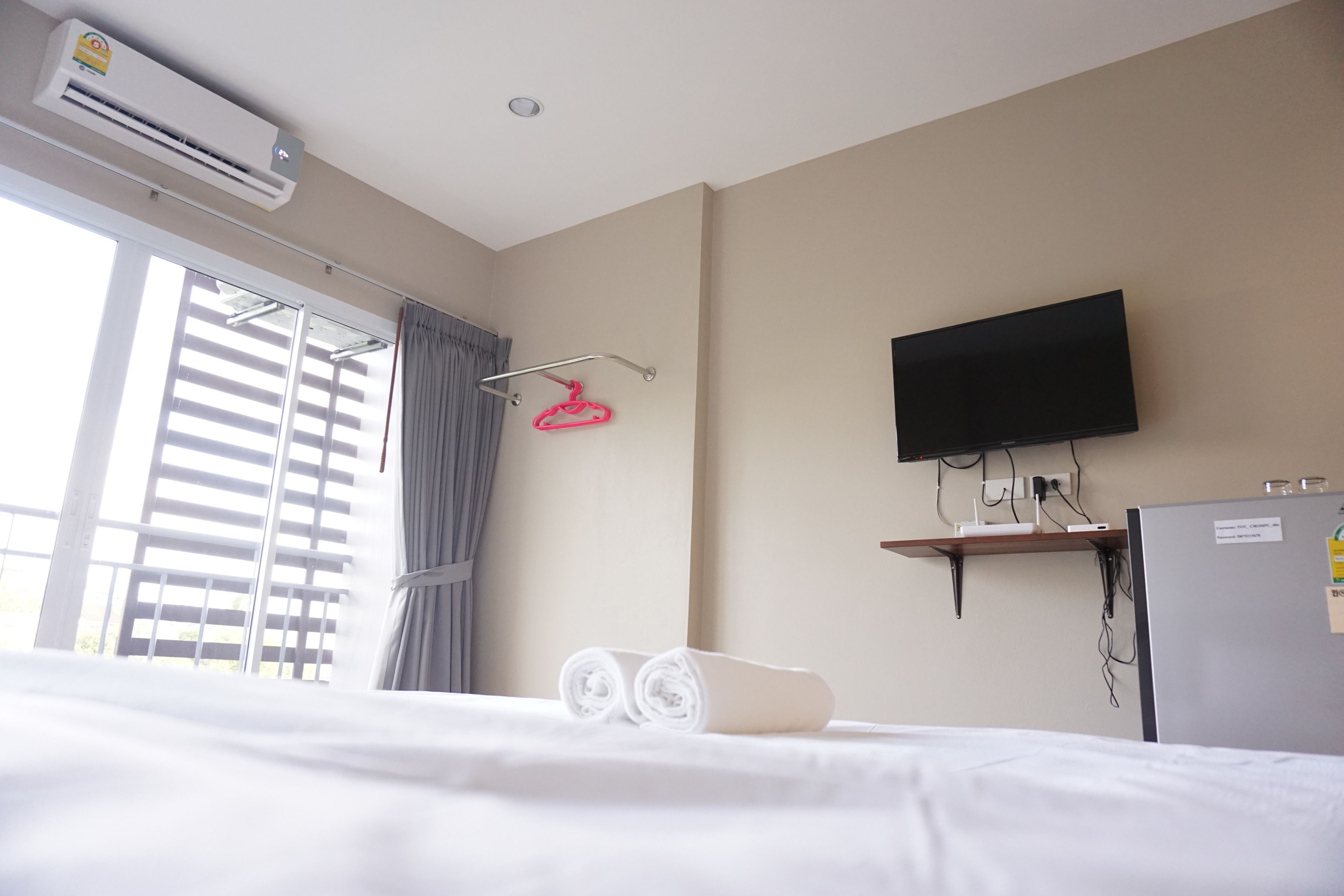 Habitación de hotel con cama, televisión montada en la pared, equipo de aire acondicionado, ventana con persianas y toallero.