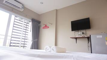 Habitación de hotel con cama, televisión montada en la pared, equipo de aire acondicionado, ventana con persianas y toallero.