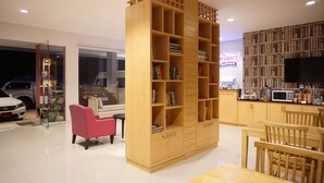 A modern living room with a large wooden bookshelf, a pink armchair, and a dining area with wooden furniture. - Chompu Nakarin Apartment (Trang)