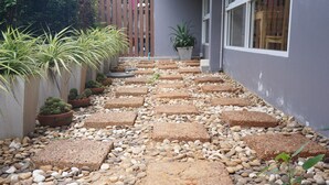 A pathway with stepping stones leading to a building entrance, surrounded by potted plants and pebbles. - Chompu Nakarin Apartment (Trang)