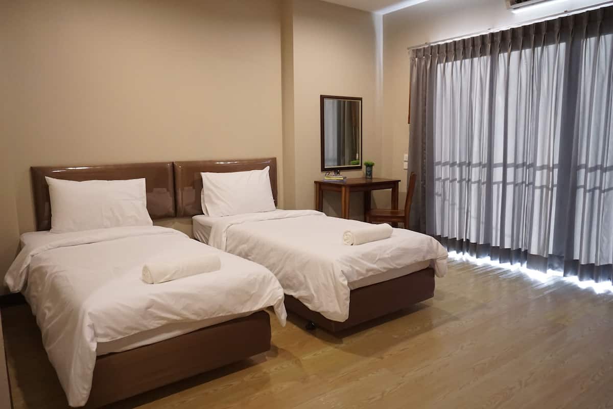 A hotel room with two beds, a small table, a mirror, and a large window with curtains.