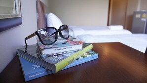 A neatly made bed, a stack of books, and a pair of glasses on a wooden nightstand in a hotel room. - Chompu Nakarin Apartment (Trang)