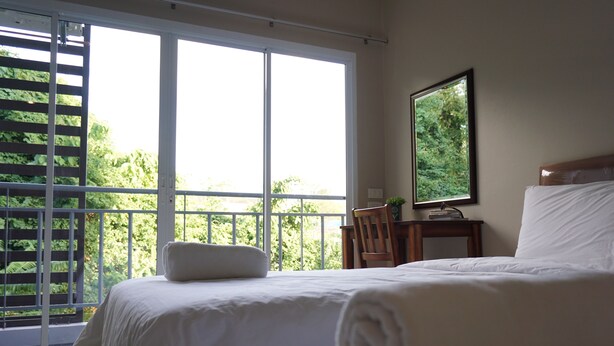 A hotel room with a large window, a bed, a chair, and a small table. - Chompu Nakarin Apartment (Trang)
