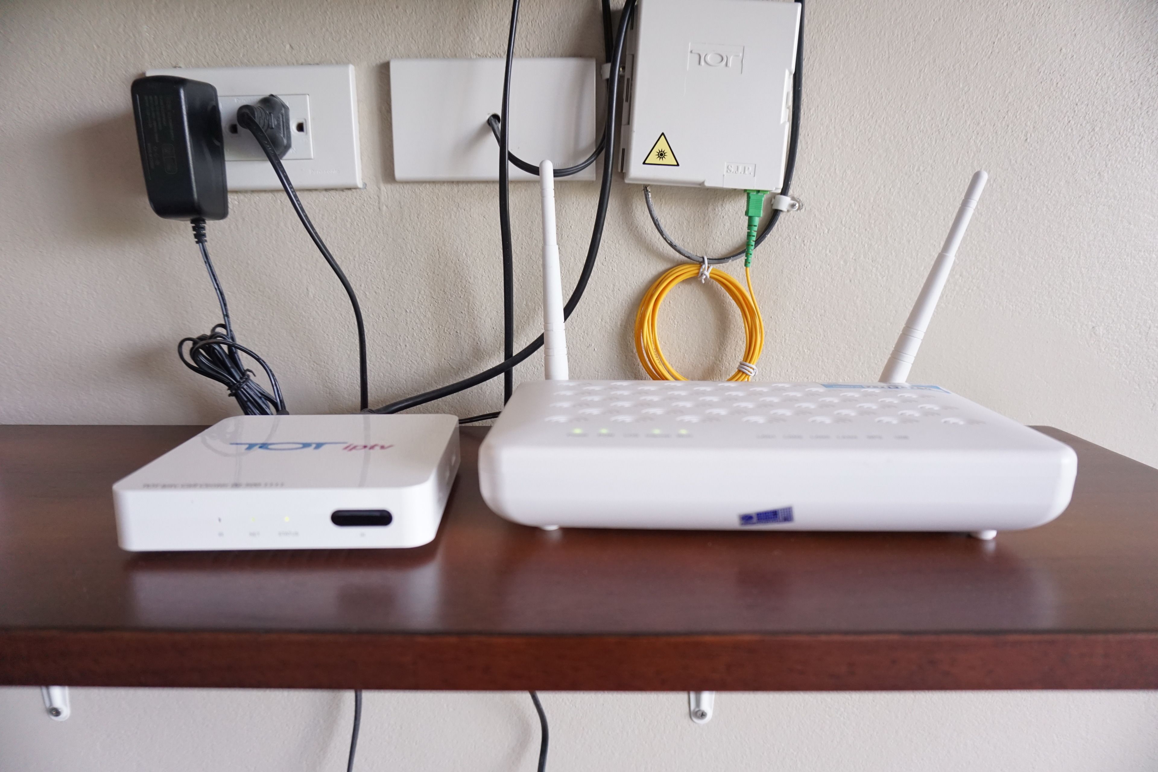 A white router and a white device on a wooden table, connected to a wall socket.