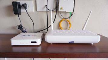 A white router and a white device on a wooden table, connected to a wall socket.