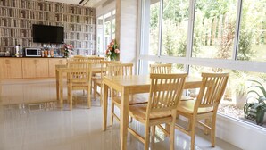 A modern kitchen with a dining area, wooden furniture, a flat-screen TV, and a view of greenery outside. - Chompu Nakarin Apartment (Trang)