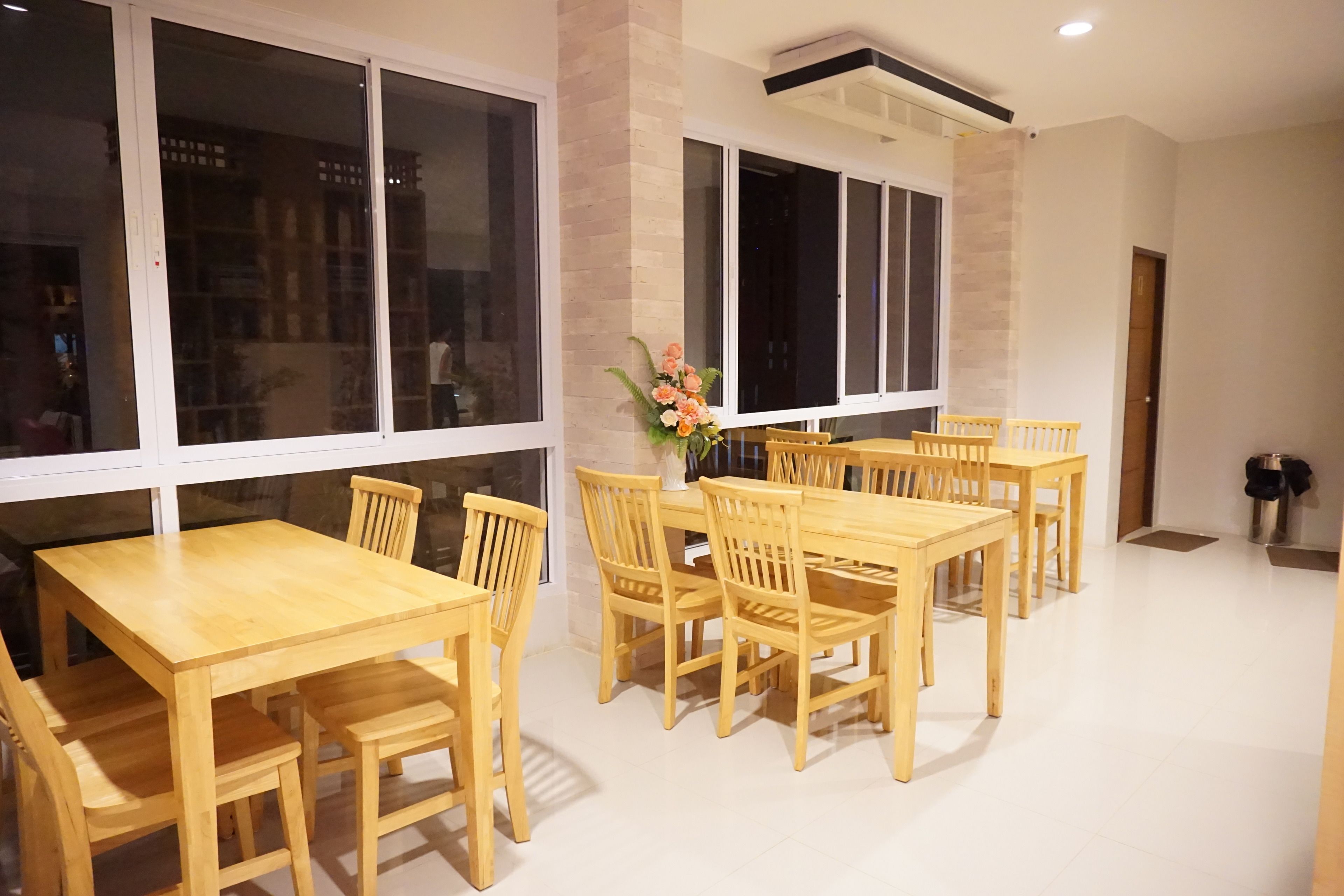Un comedor con mesas y sillas de madera, ventanas amplias y un florero con flores.