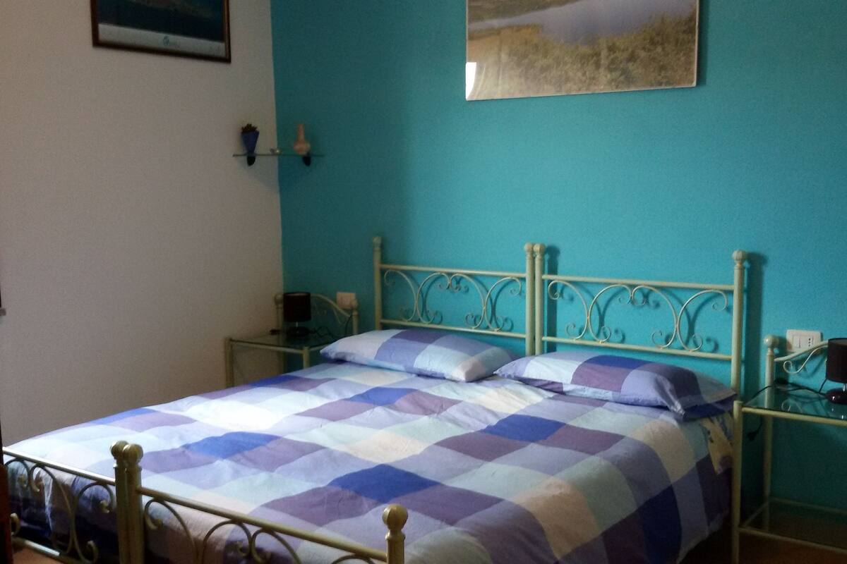 A bed with a checkered bedspread, a nightstand with a lamp, and a wall-mounted picture.