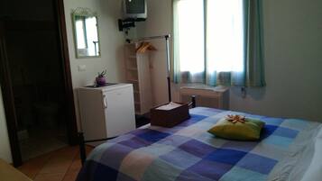 A bedroom with a bed, a small desk, a mirror, a radiator, and a window with curtains.