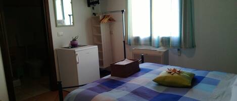 A bedroom with a bed, a small desk, a mirror, a radiator, and a window with curtains.