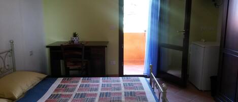 A bedroom with a bed, a desk, a chair, a television, and a door leading to an outdoor area.