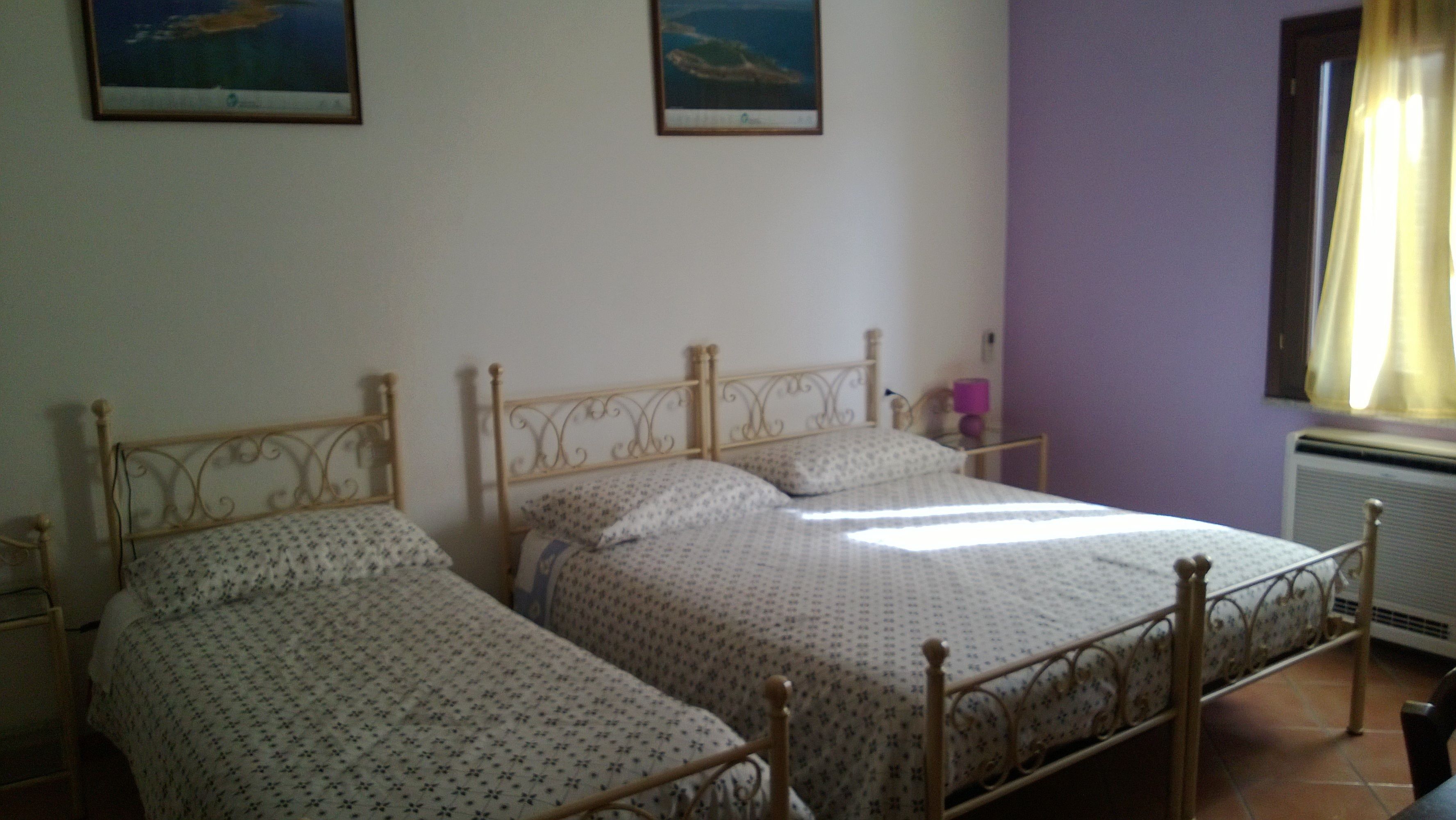 Una habitación con dos camas individuales, una mesita de noche pequeña con lámpara, y una ventana con cortinas.