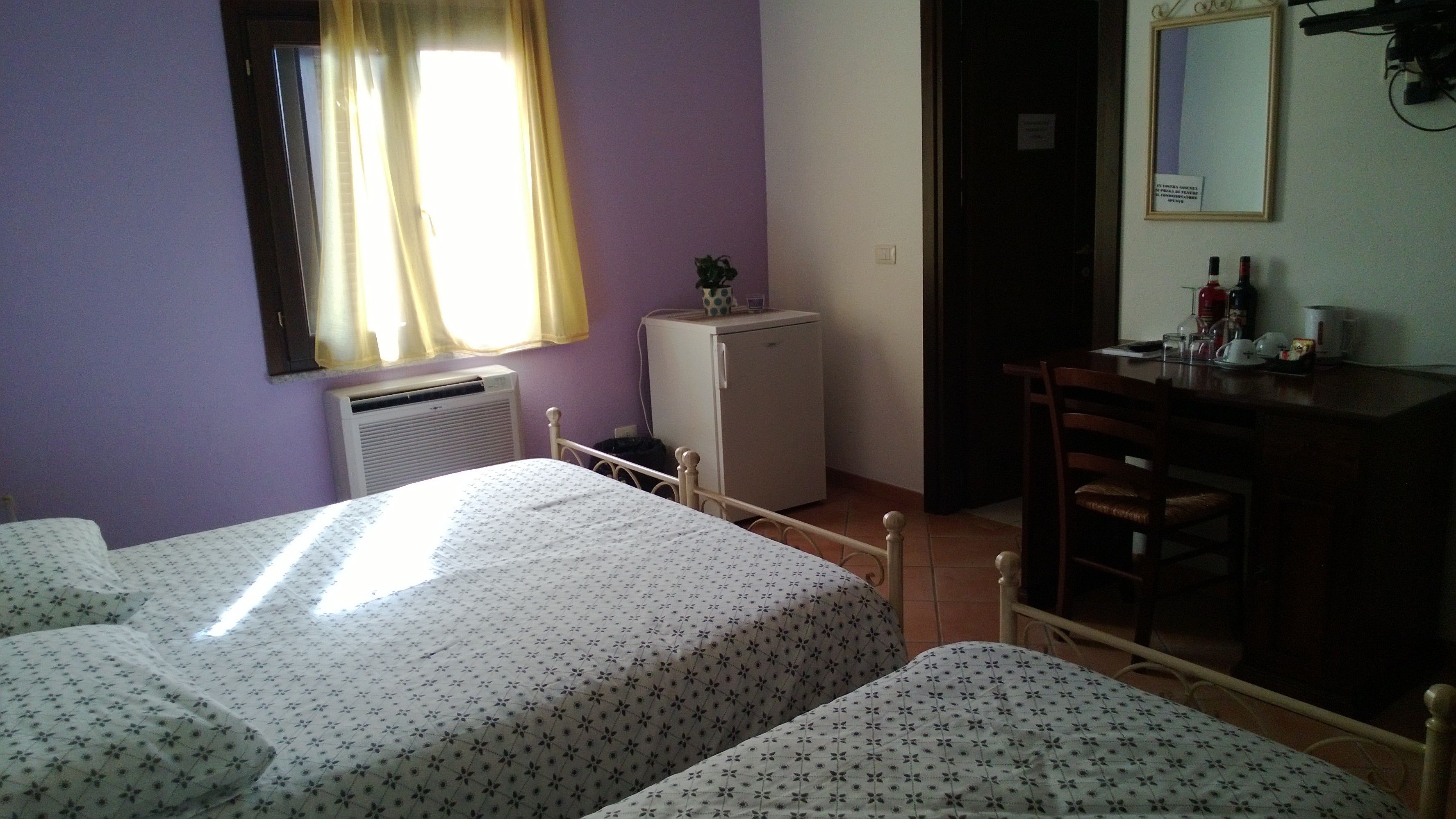 A room with two beds, a small refrigerator, a desk with a chair, and a window with curtains.