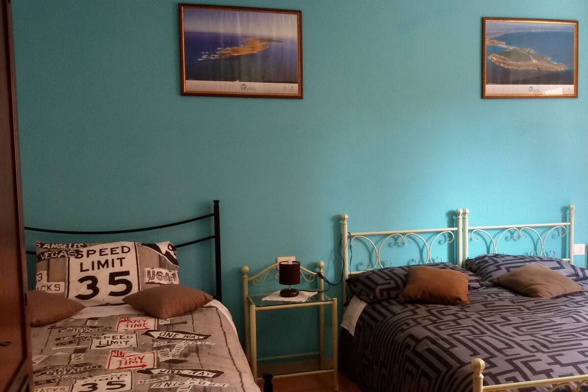 A room with two beds, each with patterned bedding and pillows. There are framed pictures on the wall above the beds.