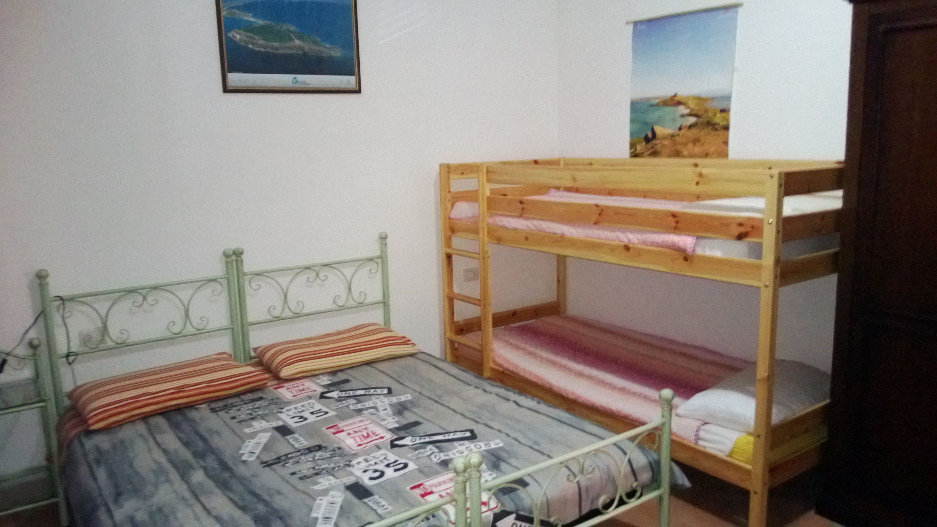 Ein Zimmer mit einem Etagenbett, einem Einzelbett mit gemustertem Bettbezug und zwei gerahmten Bildern an der Wand.