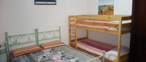Ein Zimmer mit einem Etagenbett, einem Einzelbett mit gemustertem Bettbezug und zwei gerahmten Bildern an der Wand.