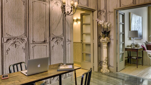 Una habitación con una mesa de madera, un ordenador portátil, un jarrón con flores y una columna de mármol.