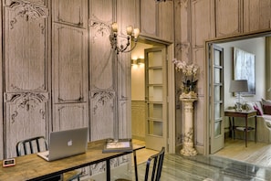 Um quarto com uma mesa de madeira, um laptop, um vaso com flores e uma coluna de mármore.