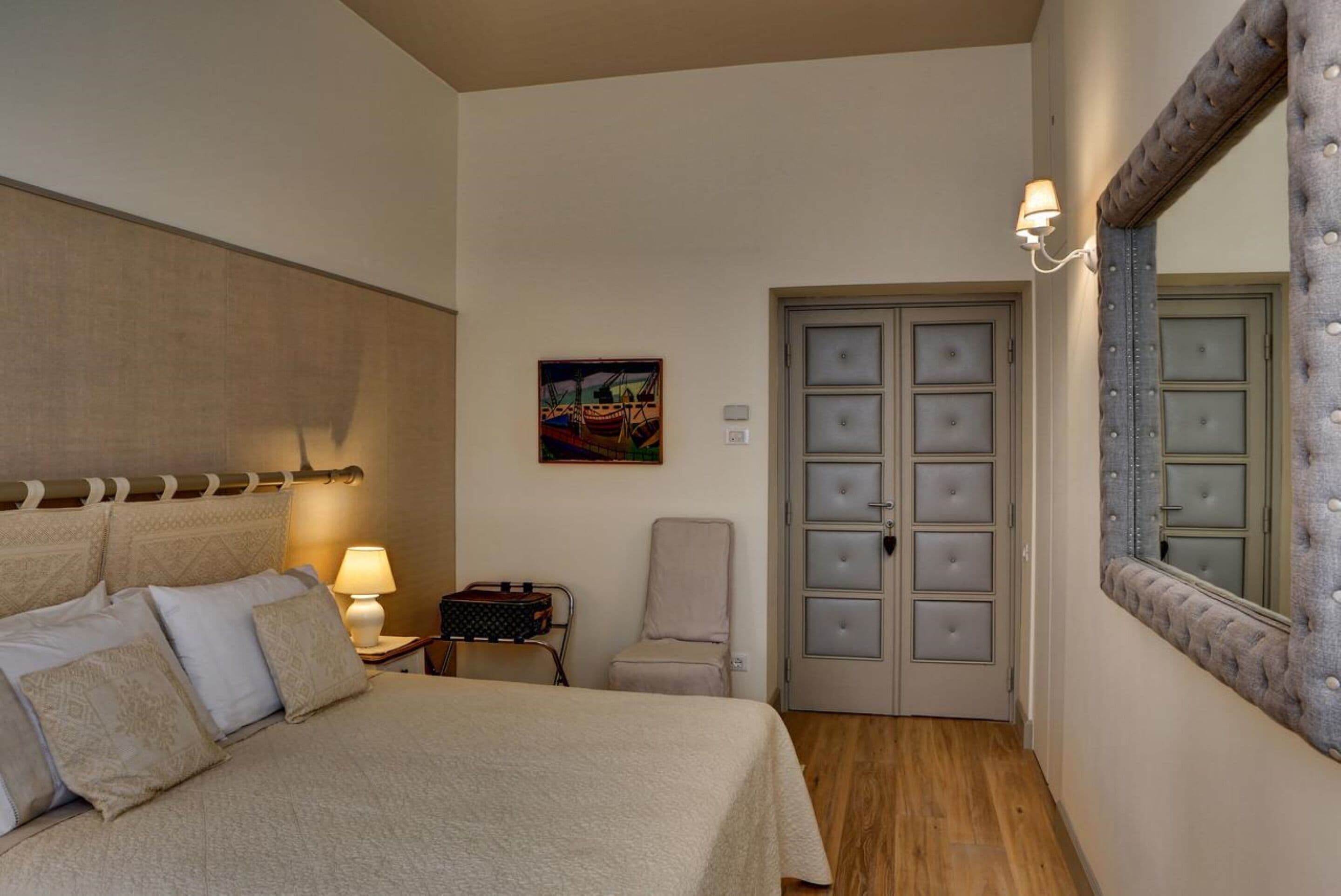 A bedroom with a bed, a chair, a dresser, a door with glass panels, and a mirror with a decorative frame.