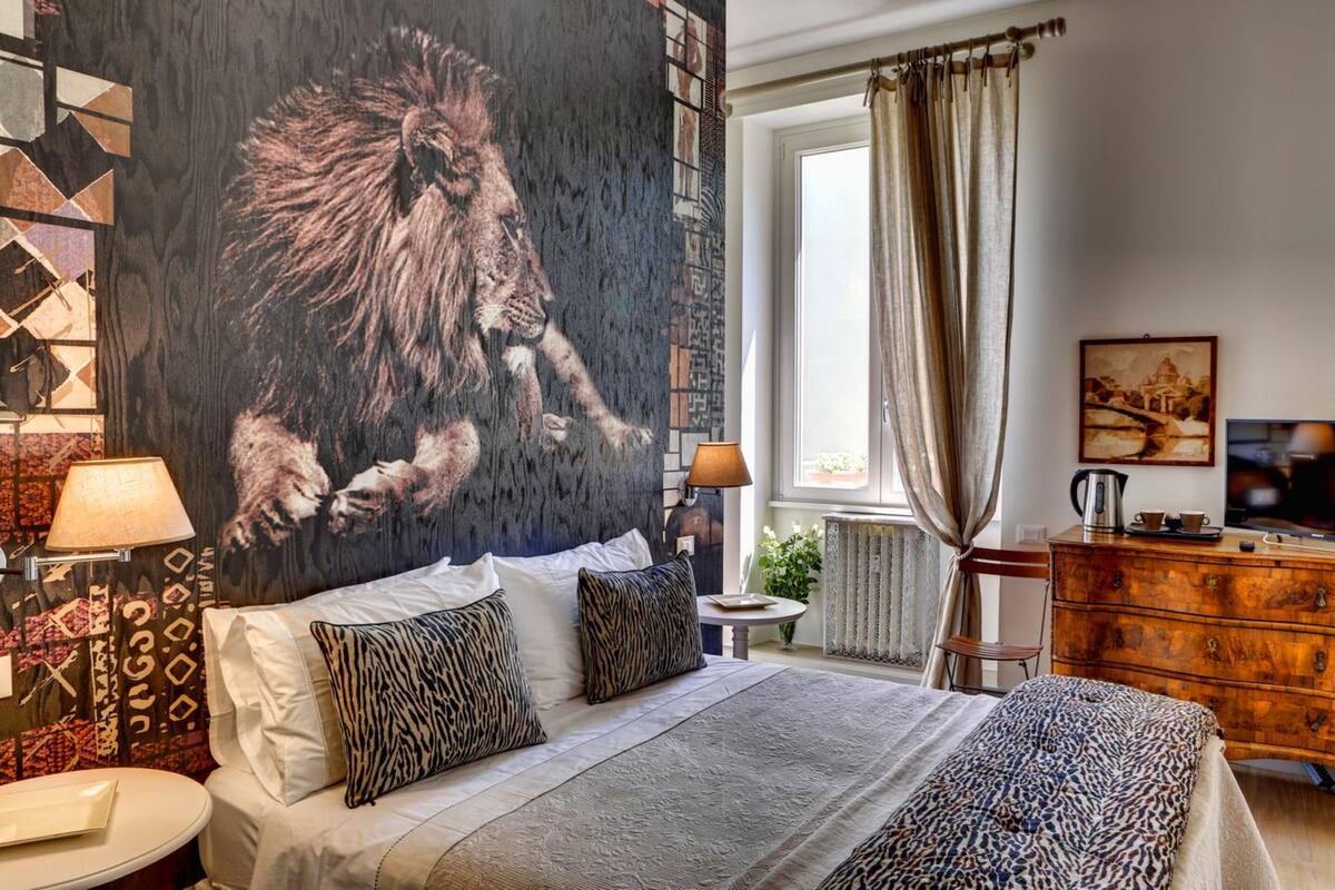 A bedroom with a large lion mural, a bed with patterned pillows, a wooden dresser, and a small table with a lamp.