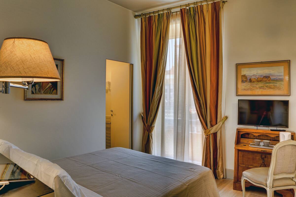 A hotel room with a bed, a desk with a television, and a chair.
