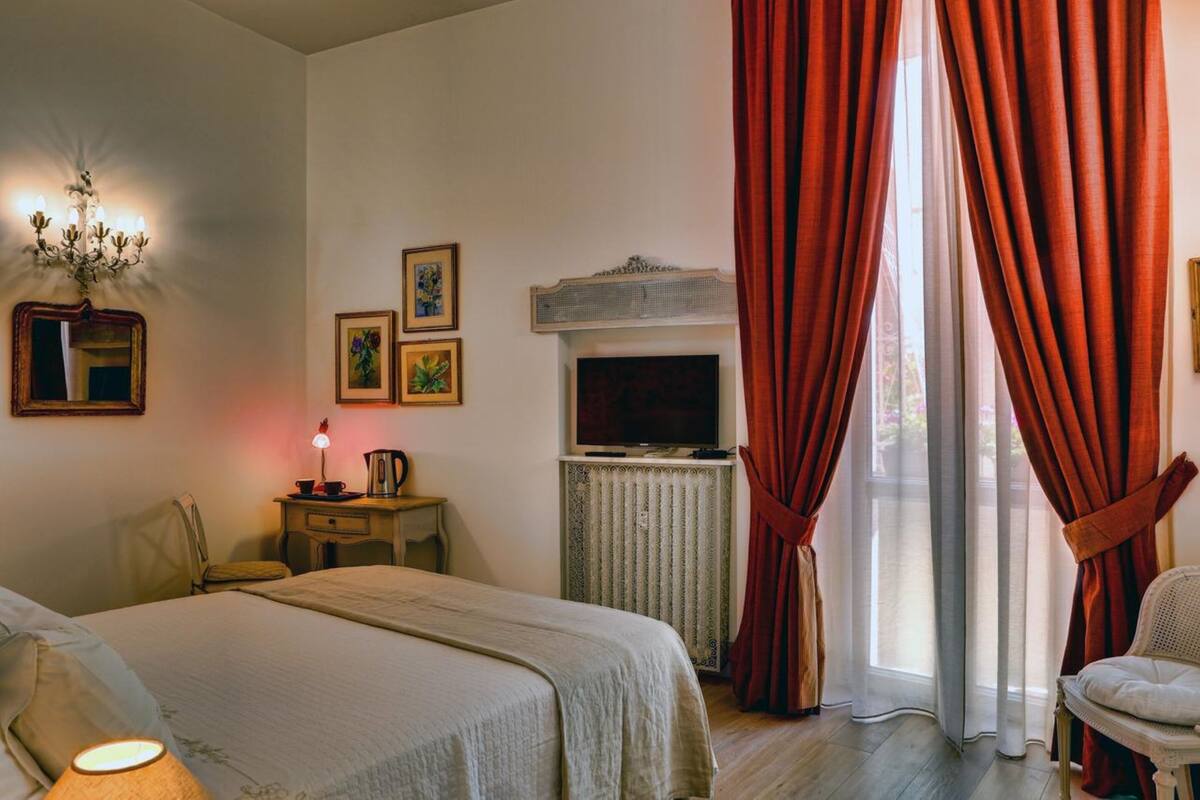 A bedroom with a bed, a television, a radiator, and curtains.