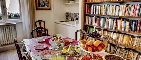 A dining table with a variety of food and drinks, surrounded by bookshelves and a painting.
