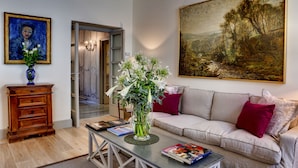 Una sala de estar con un sofá, una mesa de centro con libros, un florero con flores, un cuadro en la pared y un mueble de madera.