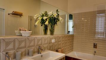 Un baño con dos lavamanos, un espejo grande y una bañera. Hay toallas y una cesta en el mostrador.