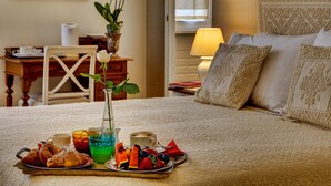 Una cama bien hecha con almohadas estampadas, una bandeja con pasteles y fruta, y un florero con flores.
