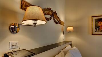 Quarto de hotel com mesa de cabeceira, luminária, quadro e espelho fixado na parede.