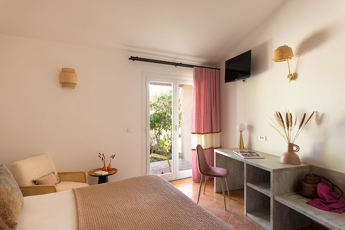 Een slaapkamer met een bed, een bureau, een stoel, een aan de muur bevestigde televisie en een schuifdeur naar een buitenruimte.