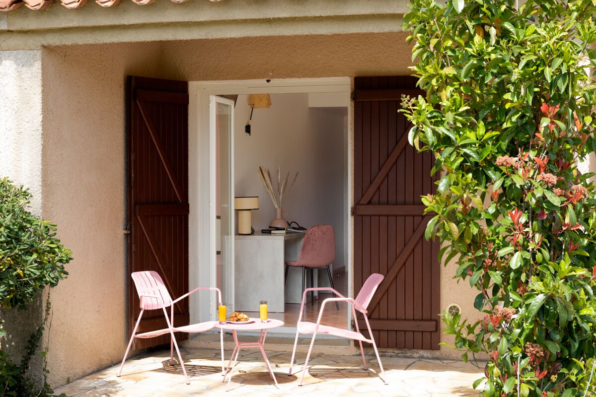 Une terrasse extérieure avec deux chaises roses, une petite table ronde et une table préparée pour le petit-déjeuner.